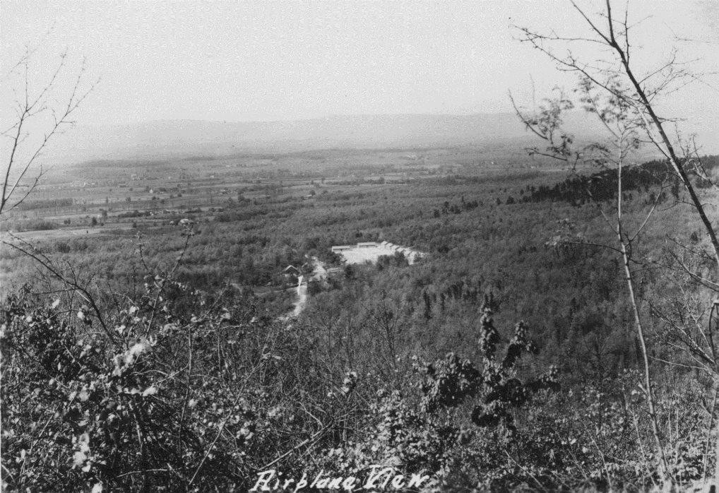 Photo of a black & white aerial photo of a camp in the mountains with barracks buildings in view.
