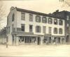 Cut stone-brick front building housing MINIUM'S MUSIC HOUSE, SINGER Sewing Machines, Dr. BASEHOAR Dentist, J. E. SIPE'S Pharmacy.