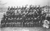 Posed group photo of the Indian School Band in uniform and holding instruments in front of bandstand.